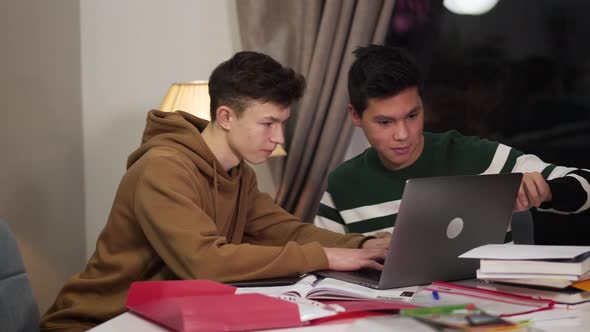 Clever Caucasian Boy Helping His Asian Friend To Deal with Laptop. Friendly Multiracial Groupmates alt