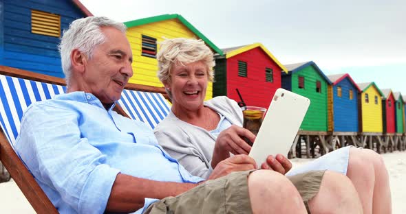 Senior couple using digital tablet at the beach alt