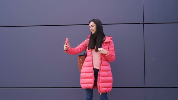 Stylish Woman in Pink Taking Selfie Against Modern Wall alt