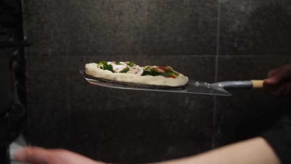 A Chef's Hand Pushes a Shovel with Raw Pizza Into an Electronic Oven