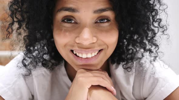 Close Up of Smiling AfroAmerican Woman Lying on Stomach in Bed Looking in Camera Laughing alt