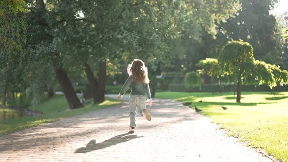 Back View Cheerful Little Girl Running in Sunshine in Spring Summer Park in Slow Motion alt