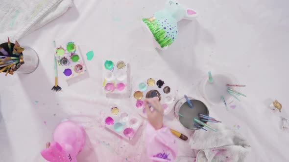 Flat lay. Little girl painting paper mache figurines with acrylic paint  for her homeschooling art p alt