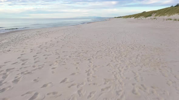 AERIAL: Very Slow Flying Above Sandy Beach with Foot Prints and Seashore on the Side alt
