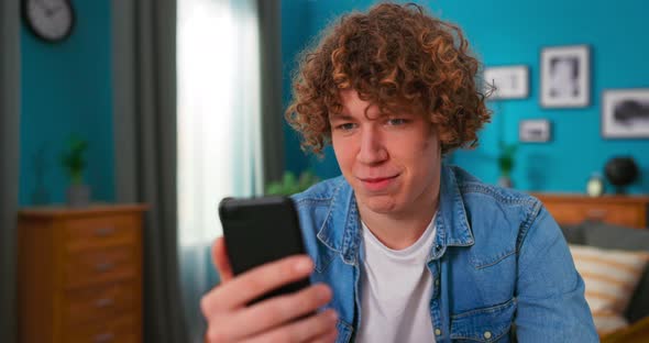 Smiling Attractive Teenager Boy Sit at Desk at Home Chatting with Friend By Smartphone Using alt