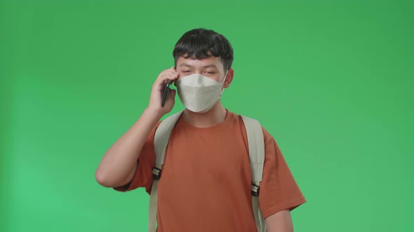 Asian Boy Student Wearing A Mask, Walking On Mobile Phone While Walking To School On Green Screen alt