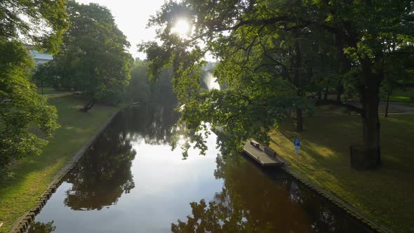 Gimbal Stabilized Tracking Shot of Park and The Riga Canal, Latvia, Warm Sun Rays Shine alt