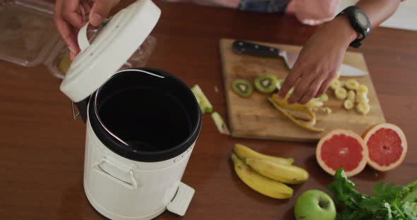 Hands of biracial man composting vegetable waste in kitchen alt