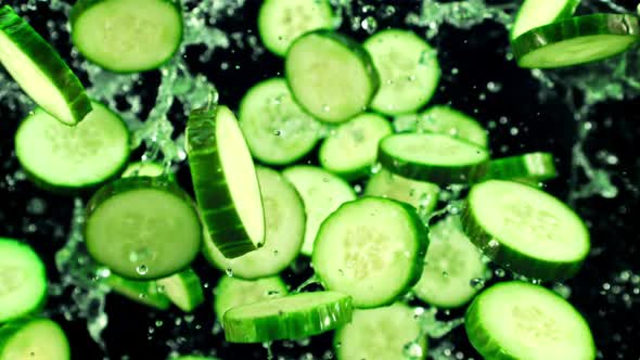 Pieces of Fresh Cucumbers with Splashes of Water Fly Up and Rotate in Flight alt