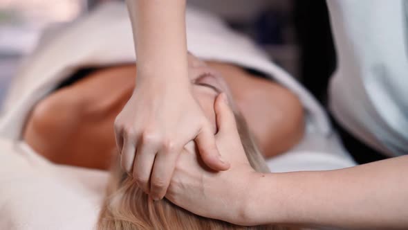 Woman masseur makes face relaxing massage to young beautiful female client blonde and spa treatment alt