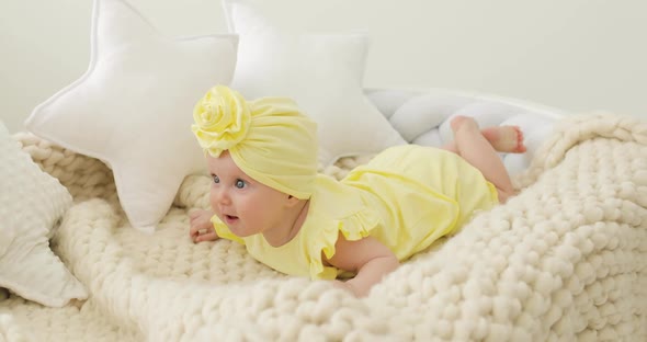 A Nice Little Caucasian Newborn Baby Girl in a Yellow Outfit and in a Turban is Lying on the White