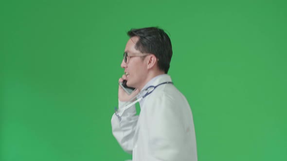 Side View Of Asian Doctor With Stethoscope Talking On Mobile Phone While Running On Green Screen alt