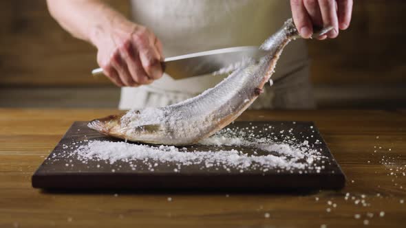 Chef Removes Salt From Herring Fish with Knife on Board alt