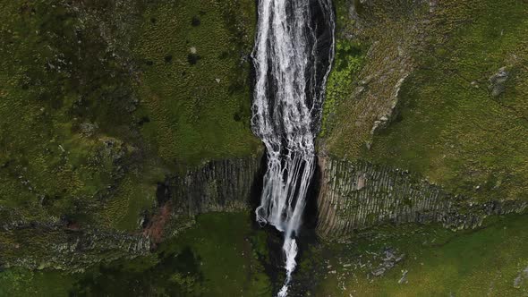 Aerial View of a Fantastic Waterfall in the Mountains Among Rocks and Green Slopes alt