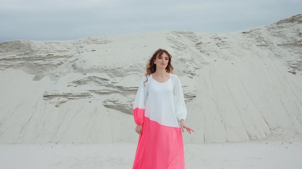Model Woman in Dress Walking on the Sand Smiling at Camera Stones in the Background alt