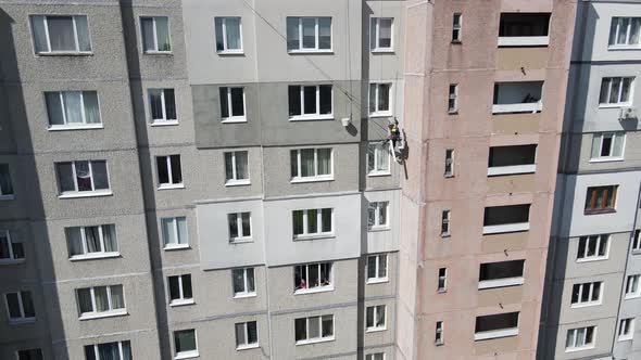 An Industrial Climber Suspended on Ropes and Paints the Wall of a Building with a Roller