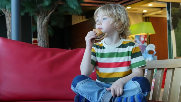 Blonde Boy Eating A Hamburger In Restaurant.