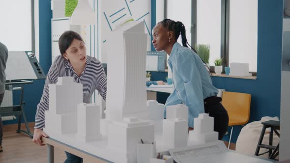 Team of Multi Ethnic Women Analyzing Maquette on Table to Design Building Model alt