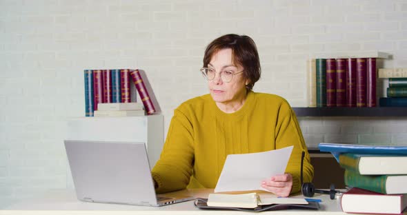 An Elderly Caucasian Woman in Glasses Works in Front of a Laptop Monitor She Checks the Tax Forms alt
