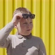 Caucasian Boy Raises Sunglasses and Looks Around Suspiciously Near Yellow Wall - VideoHive Item for Sale