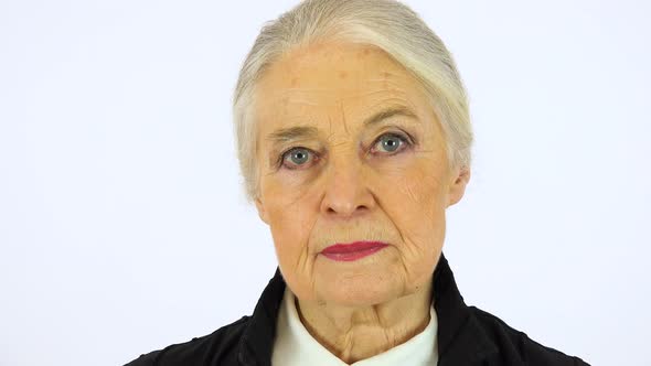 An elderly woman looks seriously at the camera - face closeup - white screen studio alt
