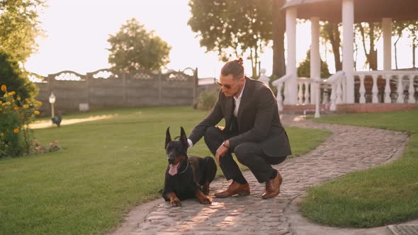 A Rich Businessman in a Business Suit Walks with a Big Doberman in the Park. A Successful Bearded alt