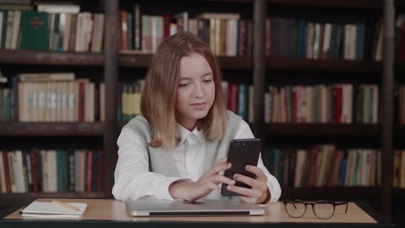 Girl in School Uniform Waving Hand Using Video Conference Call By Webcam on Smartphone Library in alt