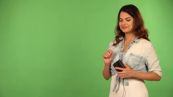 A Caucasian Woman Listens to Music on a Smartphone with Earphones on and Dances  Green Screen