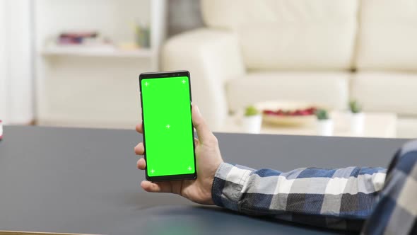 Zoom in Parallax Shot of Man Holding a Green Screen Phone on the Table alt