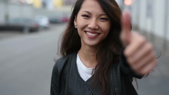 Young asian woman smiling with thumb up outdoor in the city, looking at camera alt