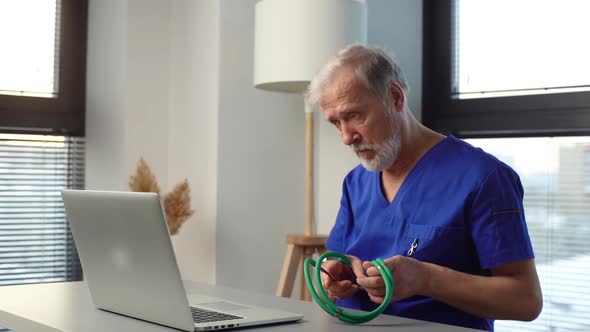 Tired Mature Male Doctor Sitting Down at Table Starting Working Typing on Laptop Computer alt