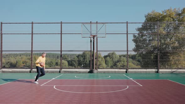 Man Trains Throwing Basketball Ball in Basket on a Street Court on a Sunny Day