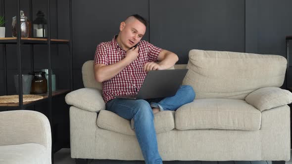 Man Freelancer Using Laptop and Talking on Smartphone