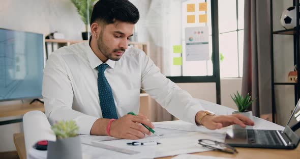 Architect Watching on Laptop Screen and Drawing Project on Large Format Paper alt