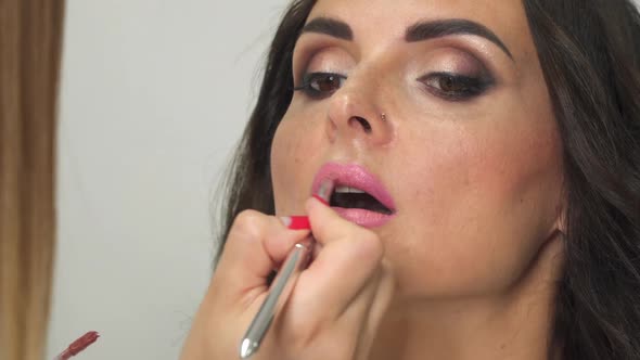 Professional make-up artist paints lips of a young woman with a brush