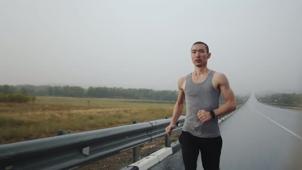 Athletic Man Runs Outdoor on Road in Steppe Doing Workout During Rain Front View alt