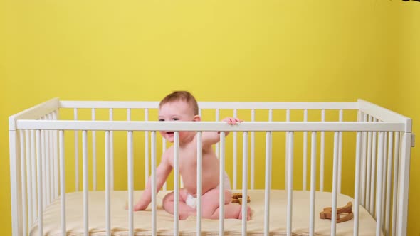 Happy infant baby boy crawls on all fours in the crib, studio yellow background. Smiling child in wh