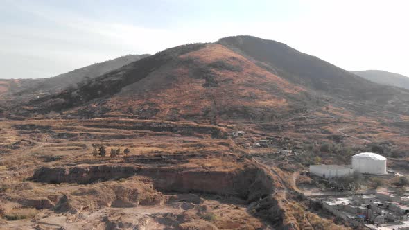 4k Aerial view of hill range beside soil excavated bare field and residential area alt