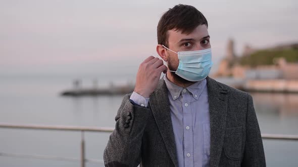 Young handsome man taking off protective medical mask during coronavirus epidemic on the street