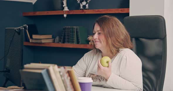 The Fat Woman is Working at Home at the Computer and is About to Eat an Apple alt