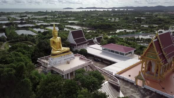 A slow orbital shot around a gold statute of sitting Buddha and a temple , Thailand. alt