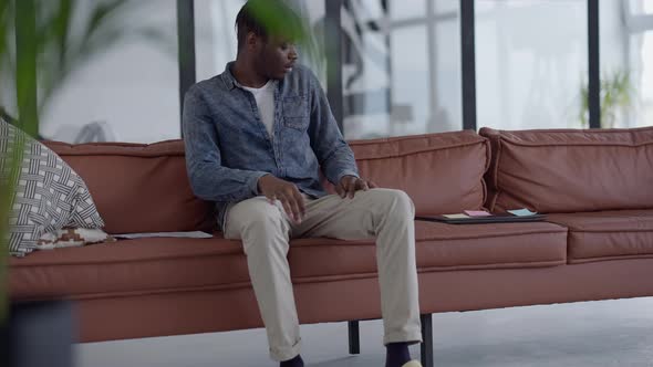 Young African American Man Walking to Couch in Living Room Sitting Down and Opening Laptop alt