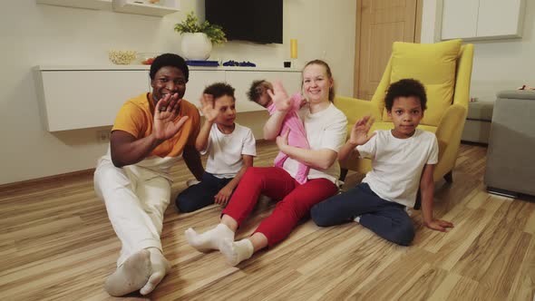 Multi Race Family Sitting on the Floor in the Room and Waving Their Hands alt
