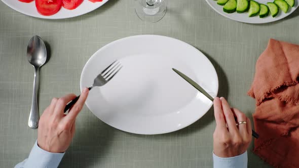 a Visitor Sits at a Table in Front of an Empty Plate in a Restaurant and Waits for an Order alt