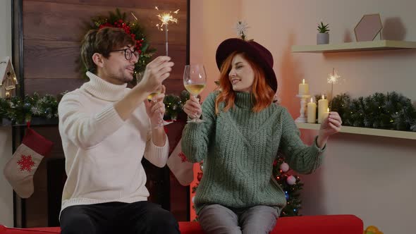Woman and a man waving sparklers and drinking shampagne on Christmas Eve. alt