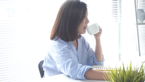 young smiling woman working on laptop while enjoying drinking warm coffee alt