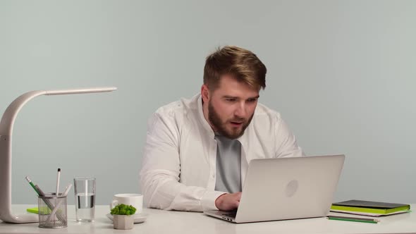 Young Successful Freelancer is Sitting at Home Office Smiling and Typing on a Laptop alt