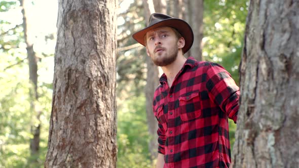 A Handsome Young Man with a Beard Carries a Tree. Stylish Young Man Posing Like Lumberjack alt