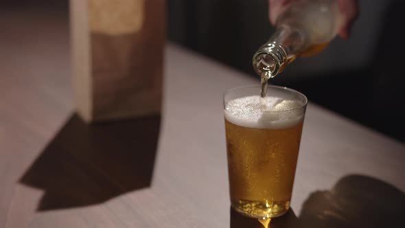 Man Pour Apple Cider in Tumbler Glass on Walnut Table with Bag of Chips on Background
