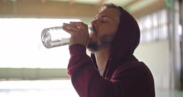 Young Adult Man with Hooded Sweatshirt Drinking Water Resting During Fitness Sport Workout